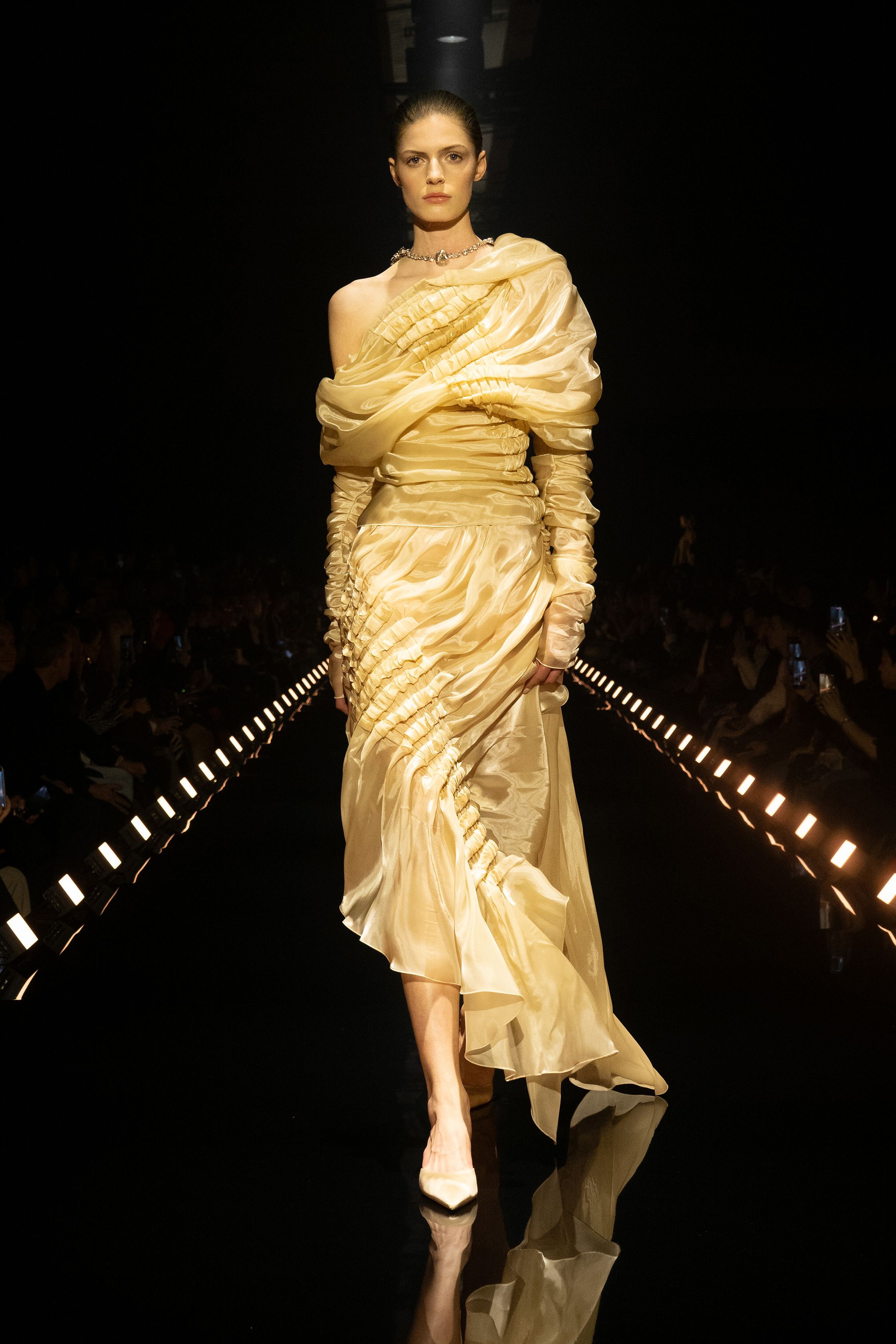 Schiaparelli 2026秋冬系列延续品牌标志性的超现实主义美学，在金色灯光的T台上呈现极具雕塑感的廓形。沙金色与黑金色成为主调，褶皱礼服、雕塑式西装与高腰裙装强化身体线条。经典的金属装饰、夸张肩线以及精致刺绣细节构成强烈视觉符号，使整场秀既华丽又充满戏剧张力。设计师通过结构与面料的张力对比，让高级定制的艺术精神融入现代女性衣橱-顽石频道趋势研究